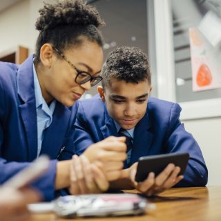 Two teen students are sneakily looking at a smart phone together during lesson time.